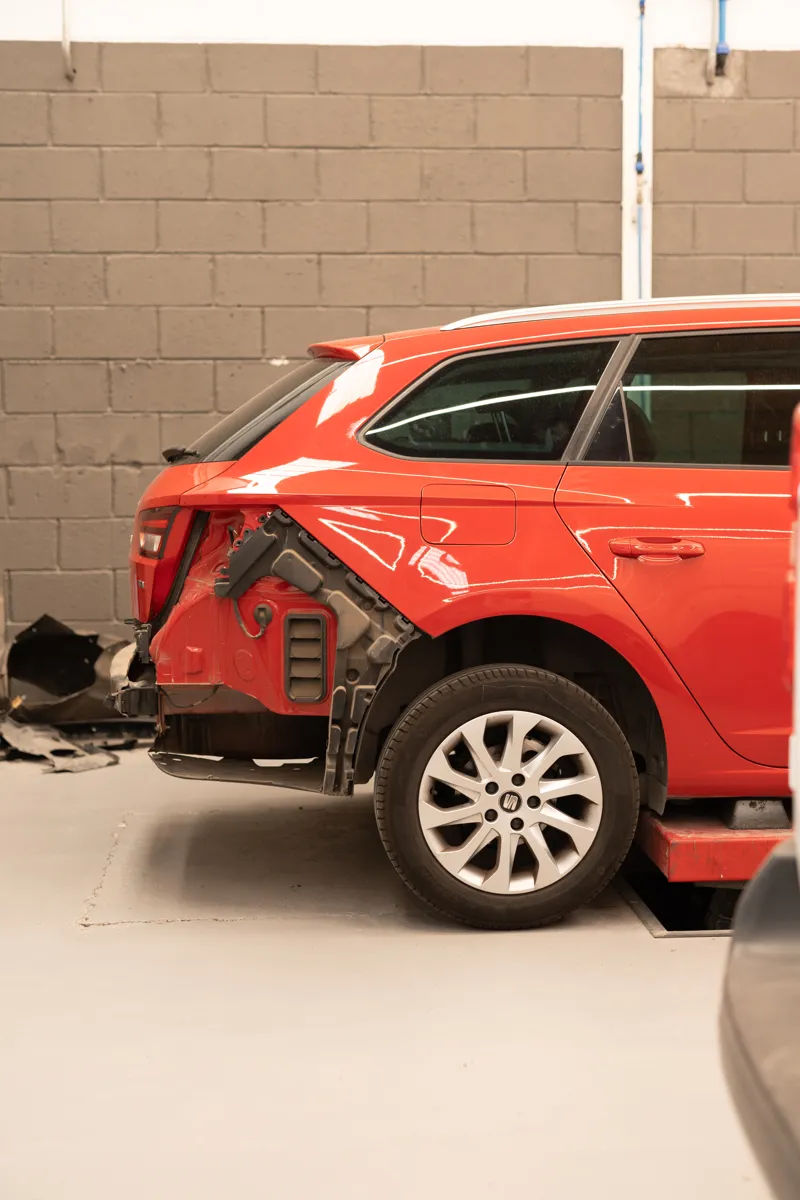 Coche rojo con la parte trasera golpeada, desmontado para su reparación en el taller