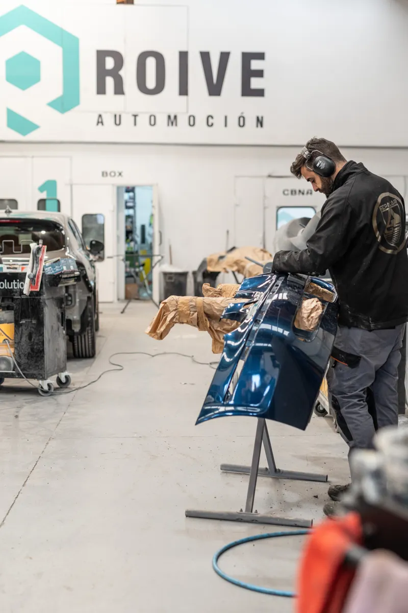 Chapista trabajando en una pieza de carrocería bajo el logotipo de Roive